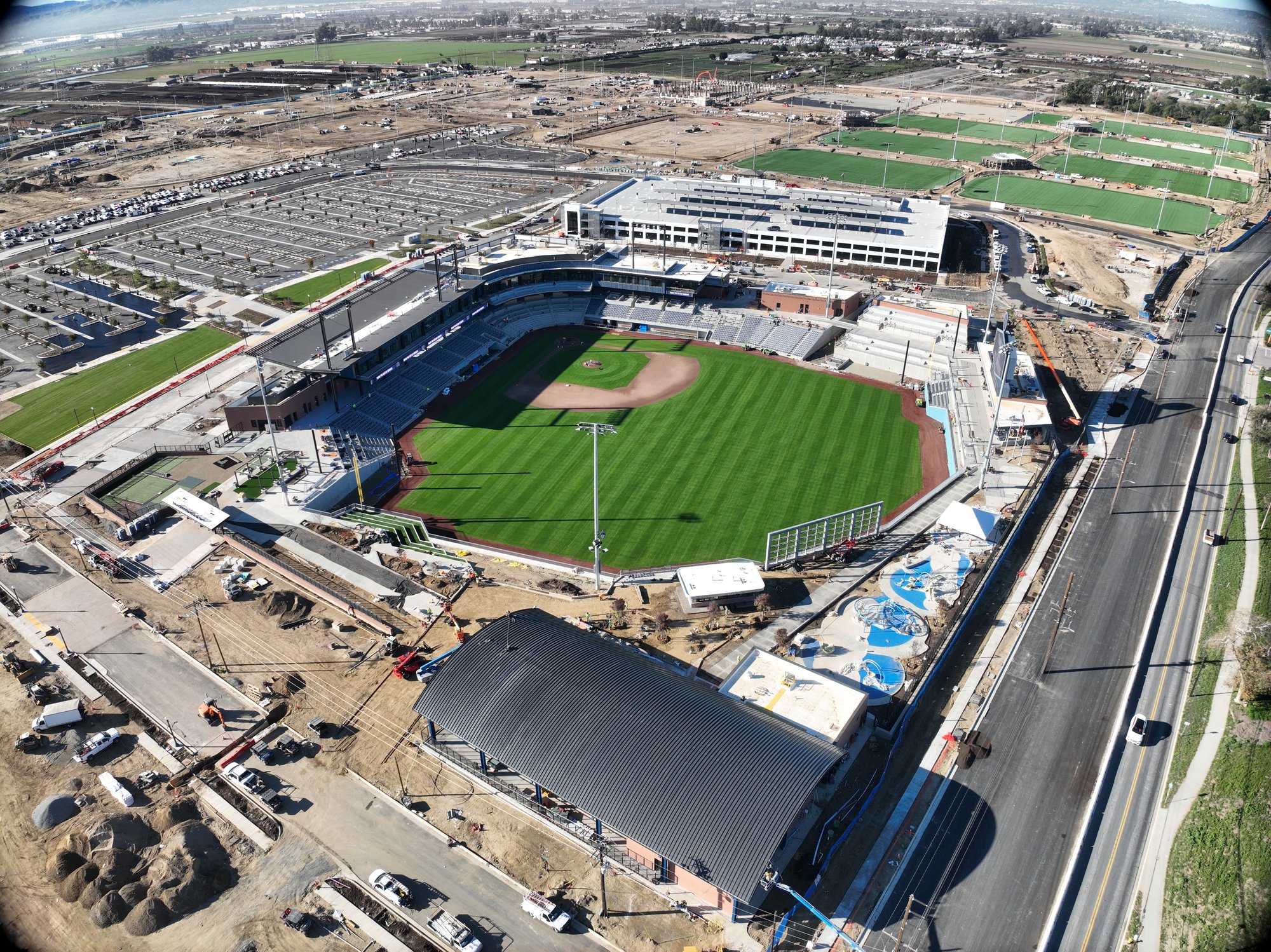 Aerial view of a baseball stadium under construction with surrounding parking lots, fields, and roadways