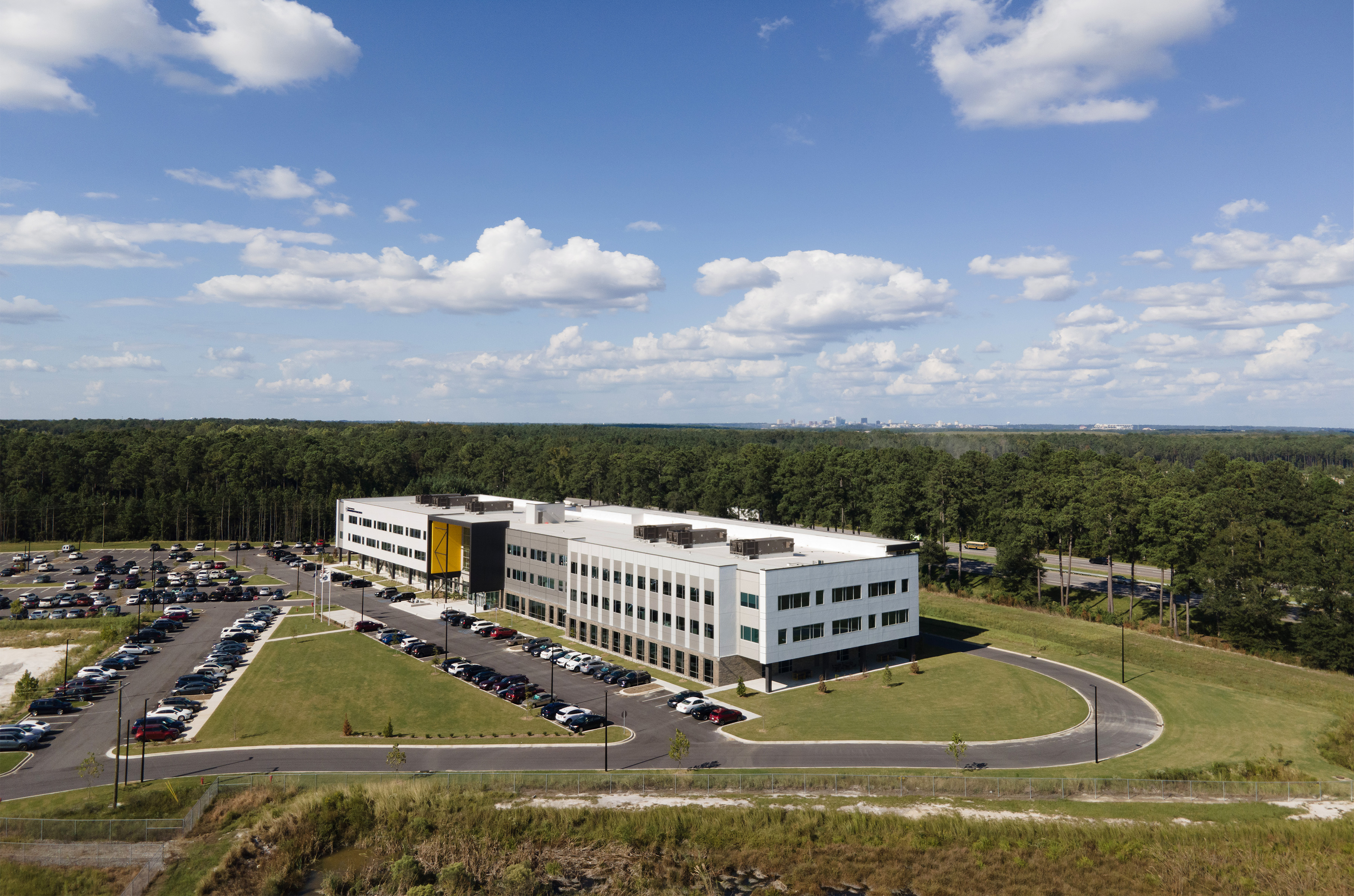 Aerial view of a modern office building with parking lot surrounded by trees under a partly cloudy sky