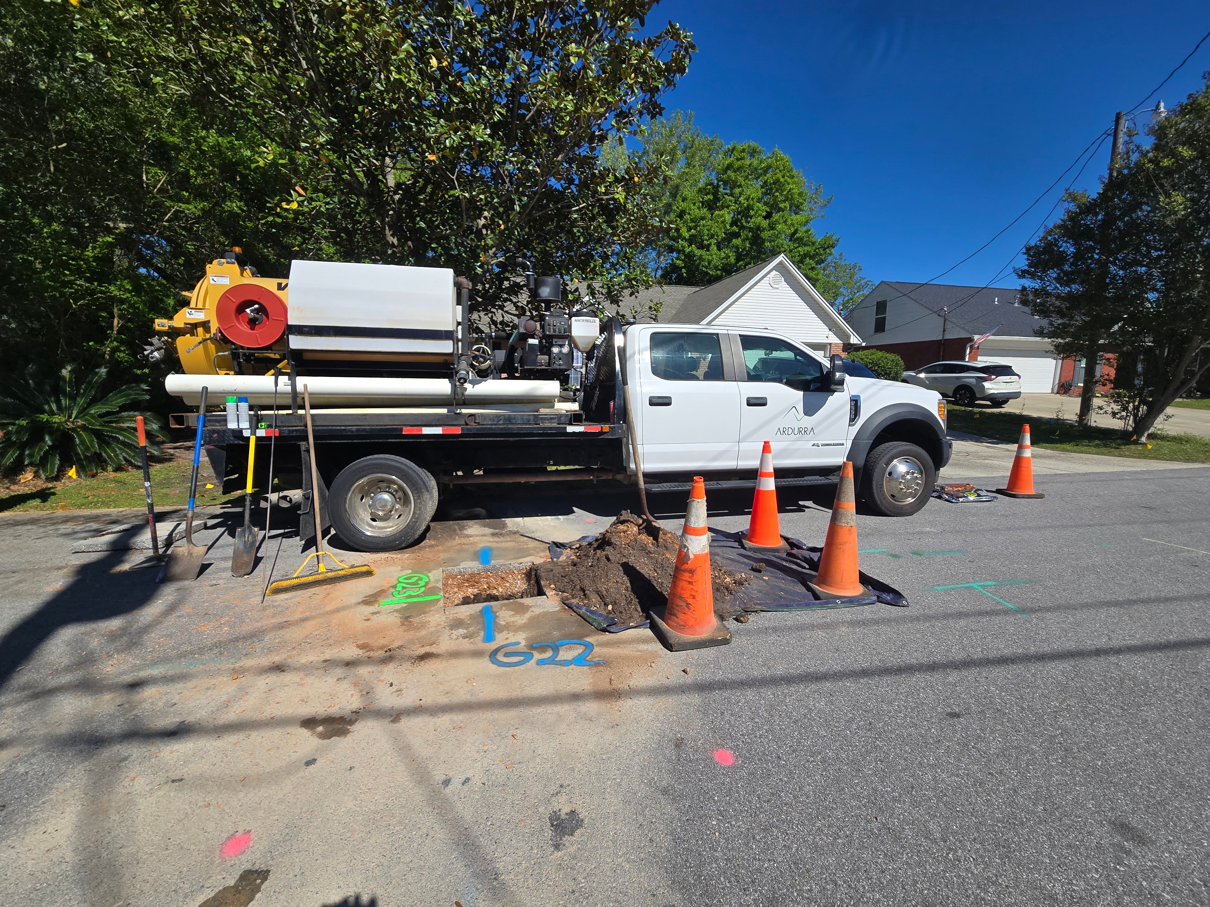 Work truck with utility equipment parked on a residential street next to an open excavation marked by cones and tools