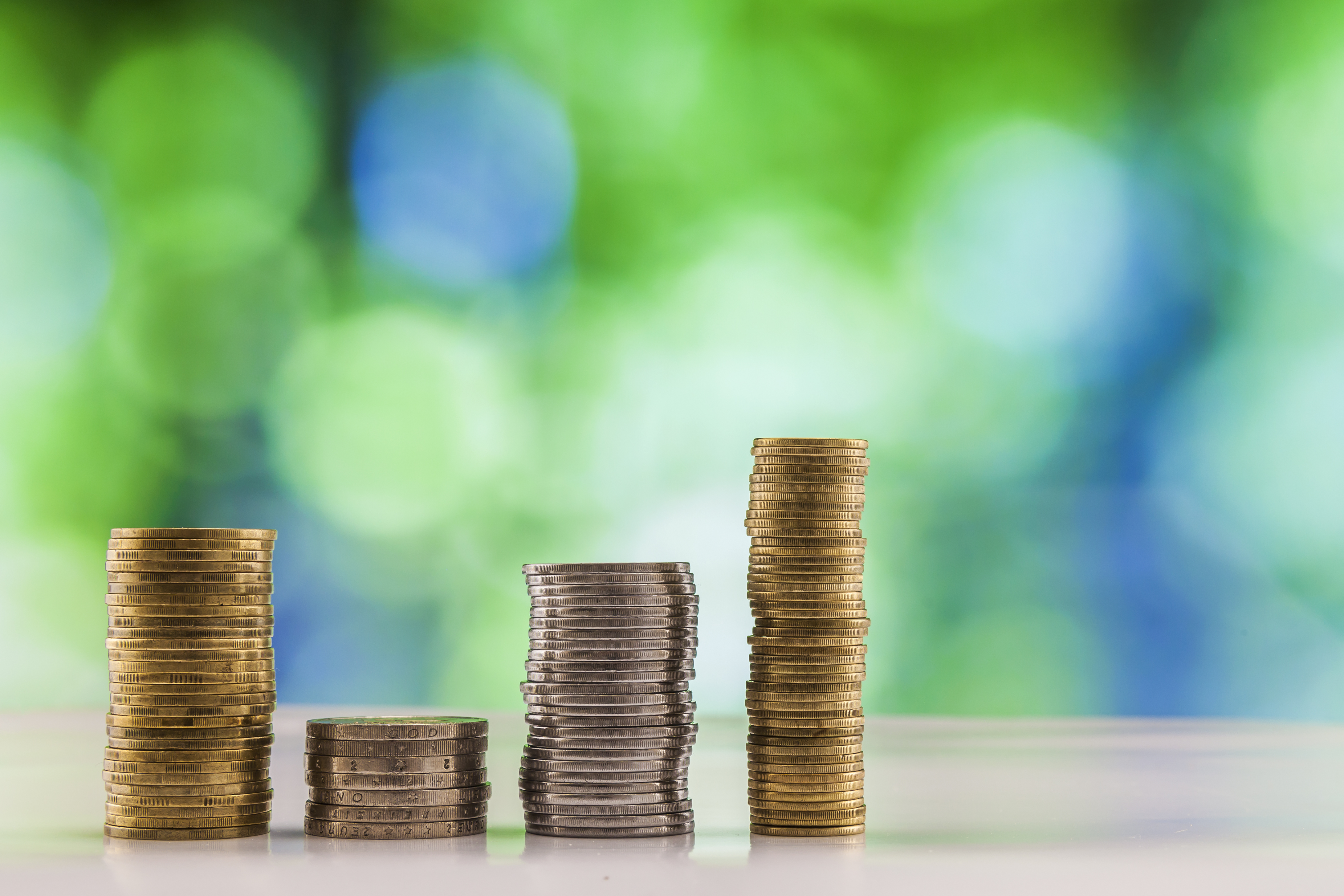 Stacks of coins of varying heights arranged in a row on a surface with a blurred green and blue background